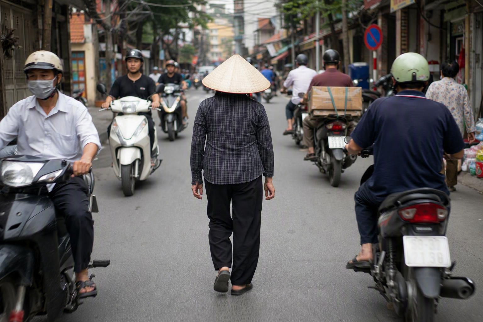 Pedestrian keeping steady pace while motorbikes pass during Hanoi street crossing