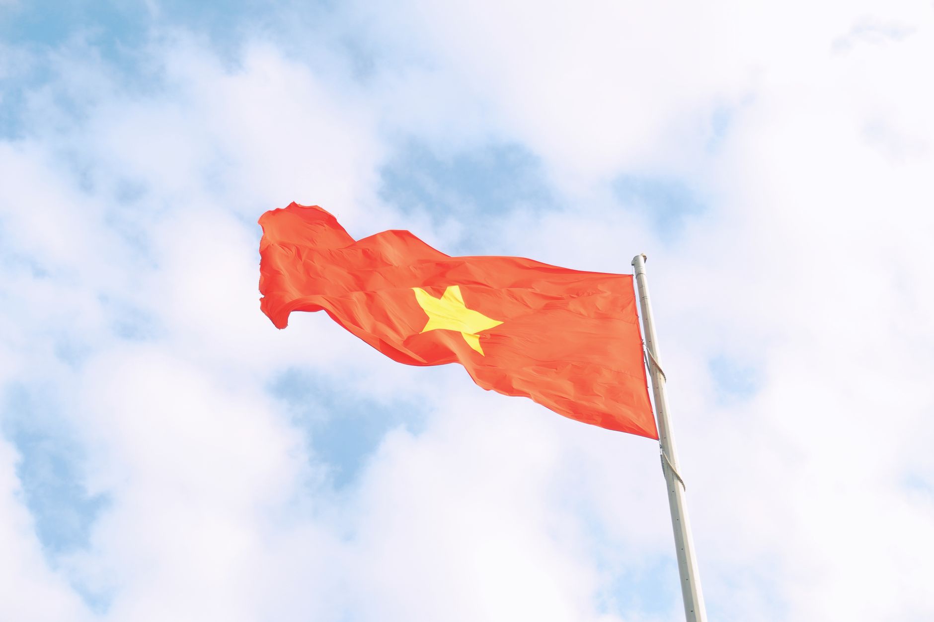 Foreign Tourism Spending in Practice — The vibrant red flag of Vietnam with a yellow star waves under a clear blue sky. (photo: Bùi Hoàng Long)