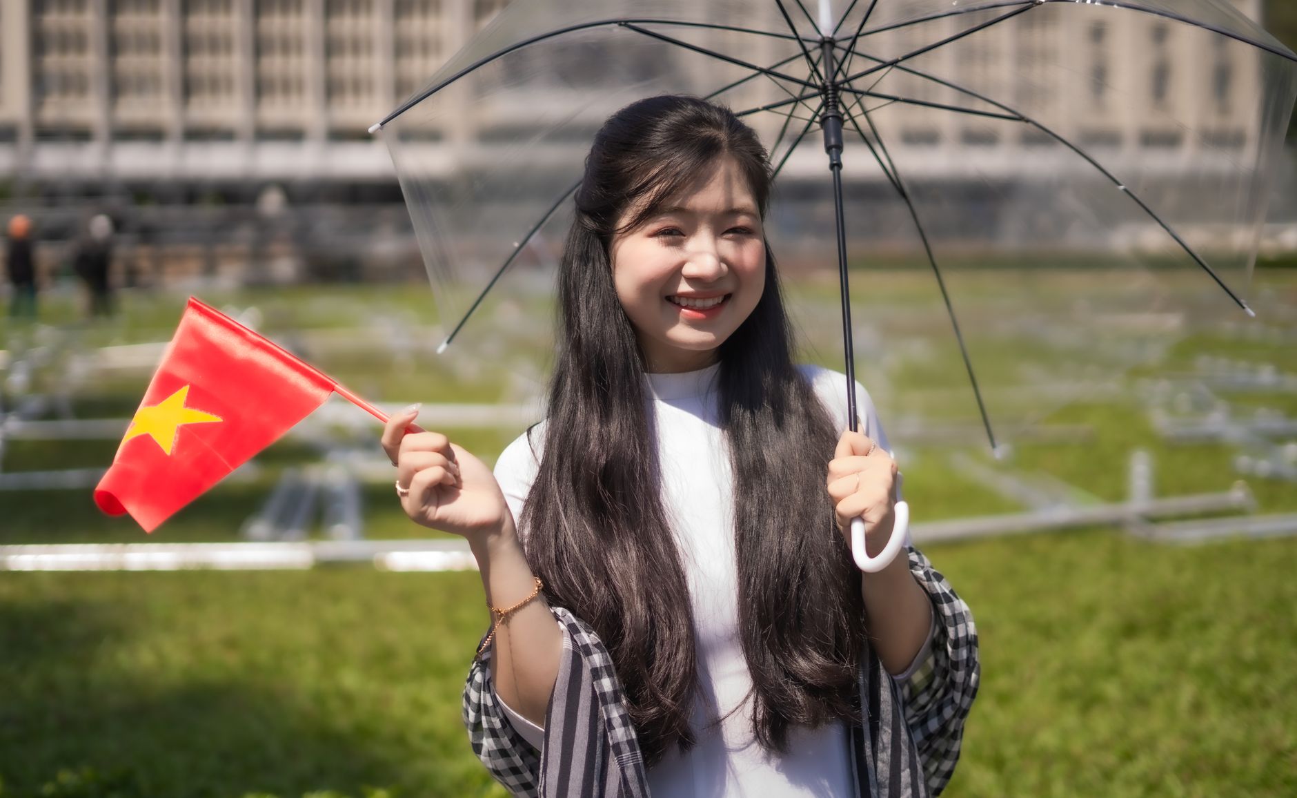 Nearby Ideas — Young woman holding Vietnamese flag and umbrella, smiling outdoors. (photo: Quý Nguyễn)