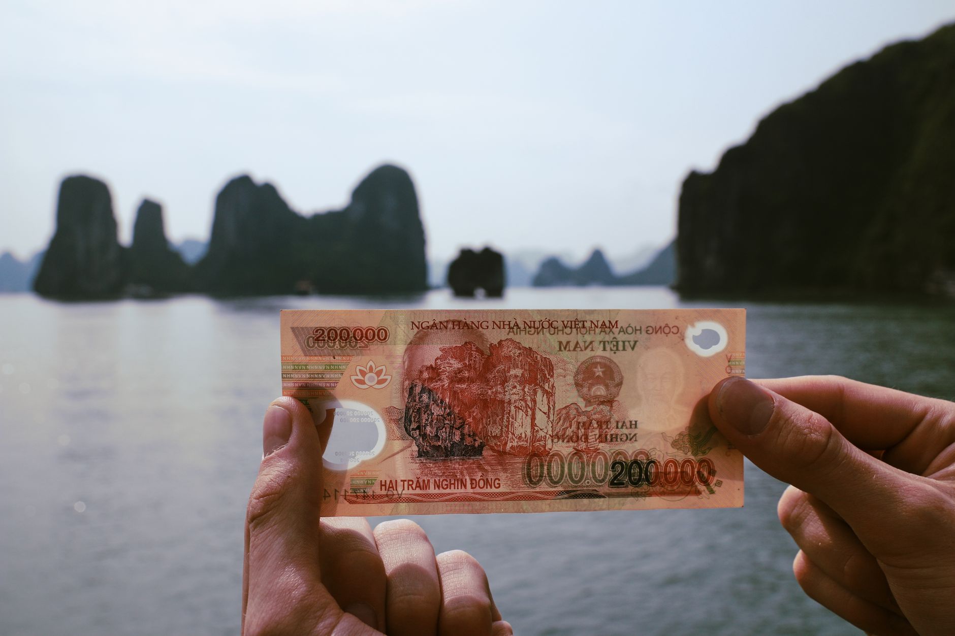 Planning Notes — Hands holding Vietnamese Dong with Halong Bay in the background, a fusion of fin (photo: My Tran)