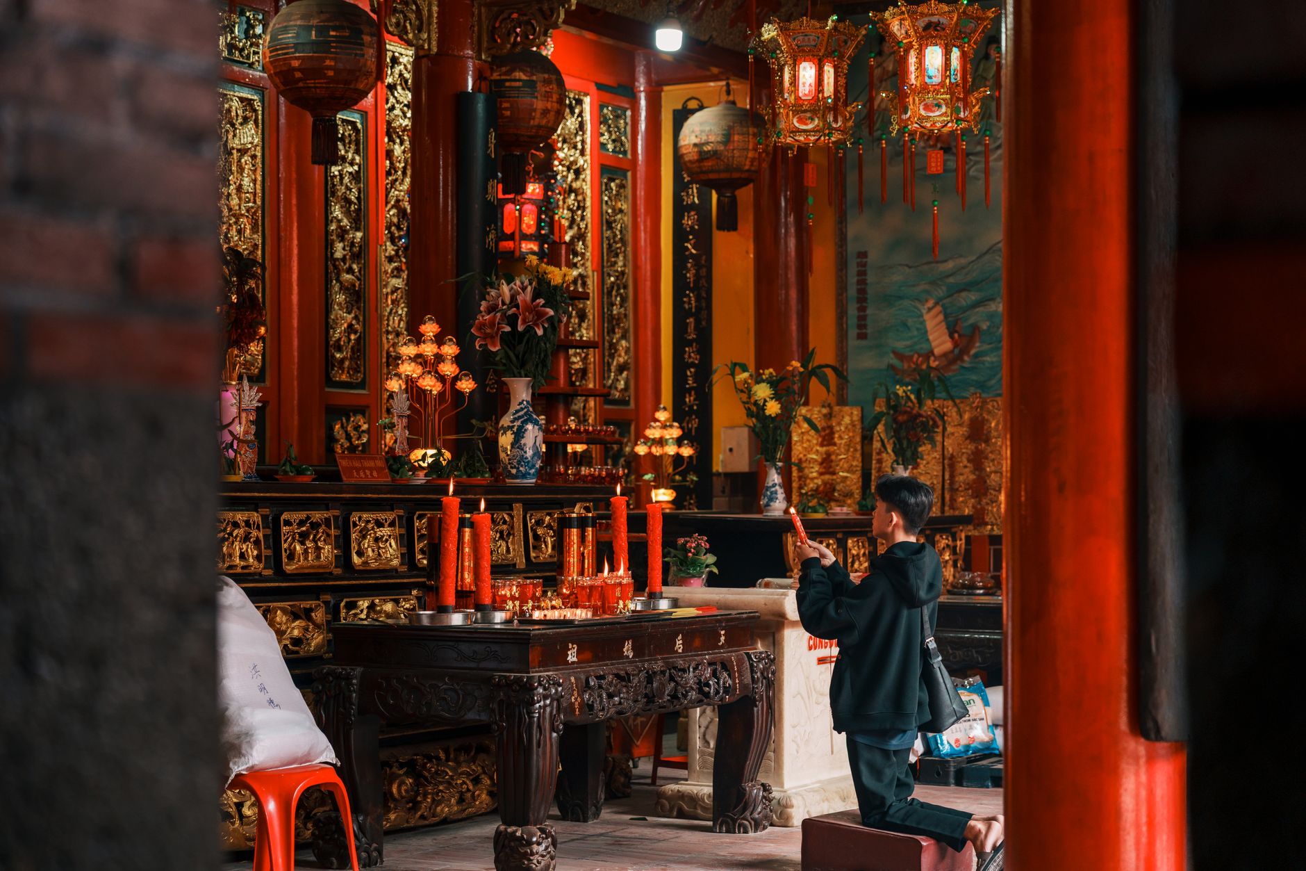 Planning Notes — A young boy praying in an ornate Vietnamese temple with red candles and lanterns (photo: Ninh Tien Dat)