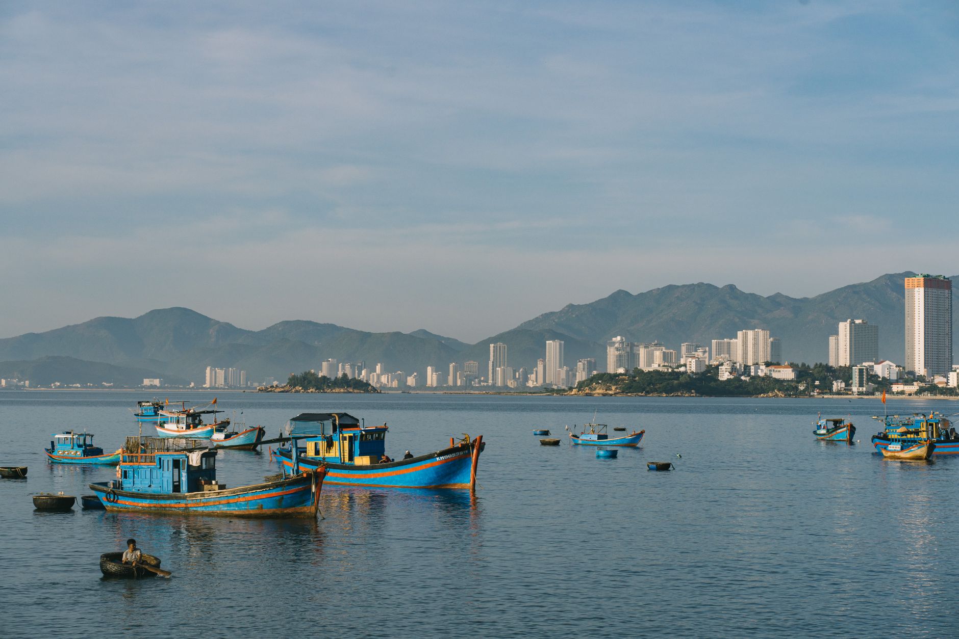 Planning Notes — Vibrant fishing boats anchored with a city skyline and mountains in the backgrou (photo: Nguyên Đoàn)