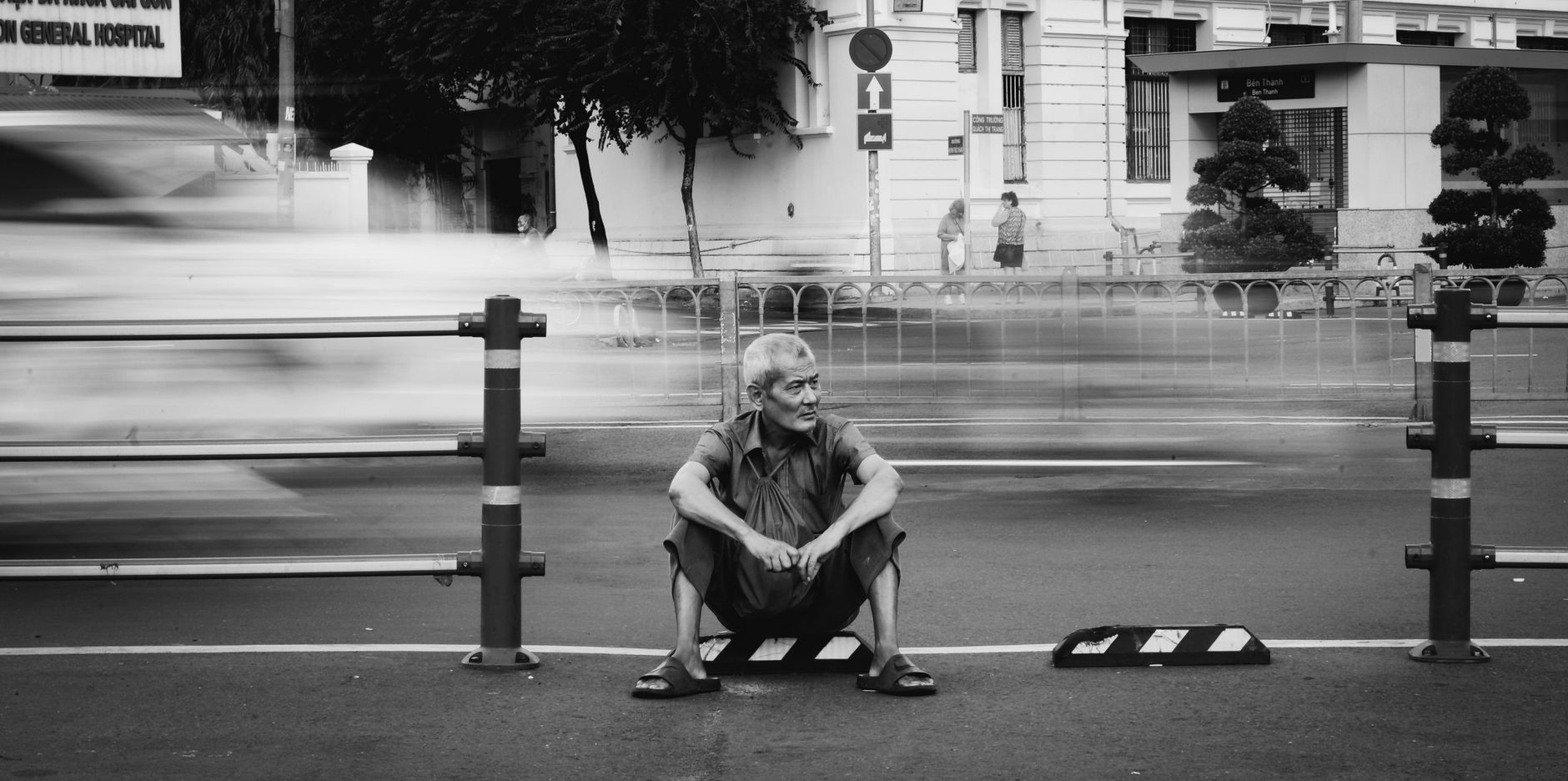 Ly Son Small in Practice — Black and white photo of an elderly man sitting on a bustling street in Vietnam. (photo: Thinh Phan Quoc)