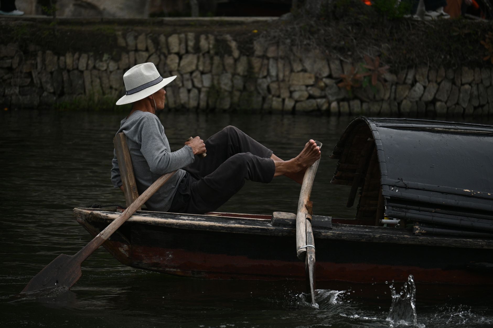 Planning Notes — A man wearing a hat rows a wooden boat in a calm river setting, with a stone wal (photo: 木 灬)