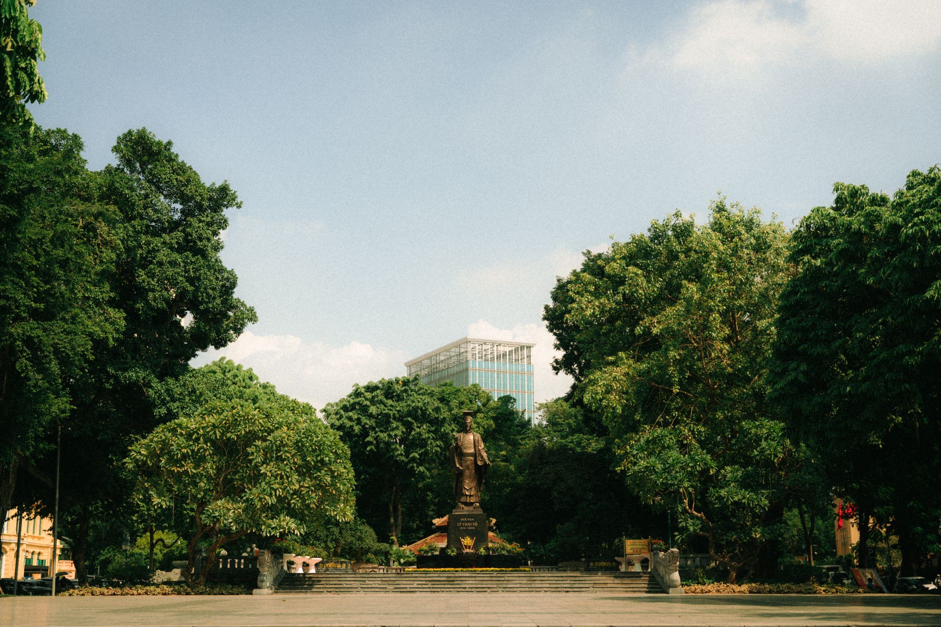 Conclusion — A statue amidst trees in an urban park with a glass building in the background. (photo: Nguyễn Quang Bảo)